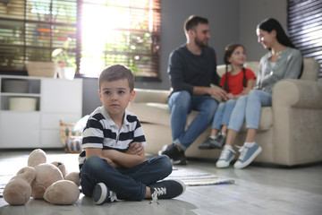 Unhappy little boy feeling jealous while parents spending time with his sister at home