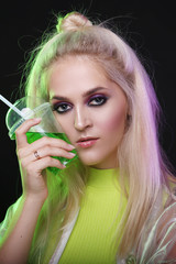 Sexy blond woman in neon light at a nightclub. With a glass of green drink, cocktail, alcohol. Nightlife. Nineties.