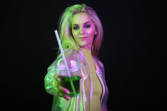 Sexy blond woman in neon light at a nightclub. With a glass of green drink, cocktail, alcohol. Nightlife. Nineties.