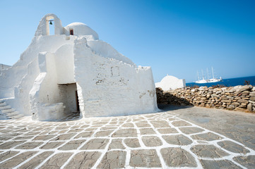 Bright sunny view of traditional whitewashed Greek architecture of Paraportiani church under bright blue Mediterranean sky