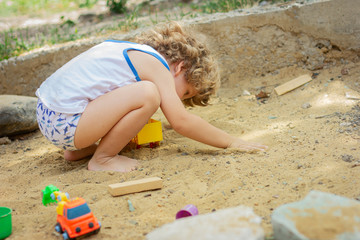 A child plays in the sandbox outdoors. A little boy is playing in the yard.