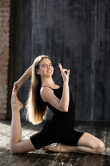 Fototapeta na wymiar A young girl in black sportswear does yoga and shows a sign ok because yoga is not complicated