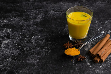 Hot healthy drink, Golden milk in a glass on a dark background, latte with turmeric with star anise...