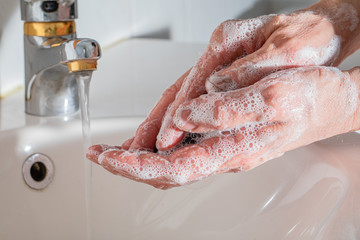 Fototapeta premium Washing hands in the bathroom, frothy soap and a running faucet in the background