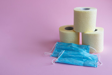 Toilet paper and medical masks on a pink background, the panic concept of the pandemic Covid-19, increased demand for masks and toilet paper