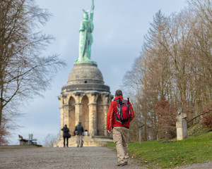 Obraz premium A hiker with a backpack and hiking poles in winter in Germany. The man approaches the Hermann Monument, which is near the Westphalian city of Detmold.