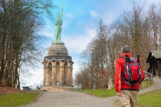 A hiker with a backpack and hiking poles in winter in Germany. The man approaches the Hermann Monument, which is near the Westphalian city of Detmold. The sky is blue.