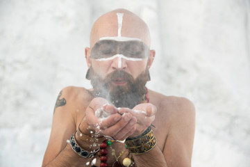 young man with primal makeup and beads spells with powder in hands on white rocks