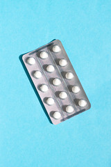 White pills in a blister pack on the blue background top view close up