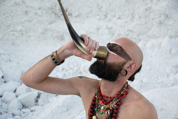 young man with primal makeup and beads spells with powder in hands on white rocks