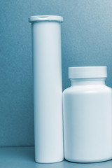 2 white vials without labels for medicines, vitamins, liquids are on a gray shelf. mockup for pharmacy and store design. blue tinting