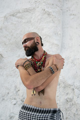 young man with primal makeup and beads spells with powder in hands on white rocks