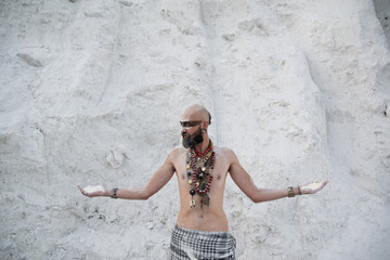 young man with primal makeup and beads spells with powder in hands on white rocks