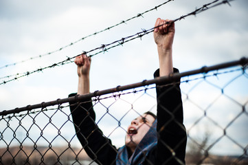 The migrant is holding his hands behind the protective fence