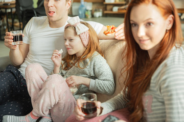 Family spending nice time together at home, looks happy and cheerful. Mom, dad and daughter having fun, eating pizza, relaxing while sitting on sofa. Togetherness, home comfort, love, relations