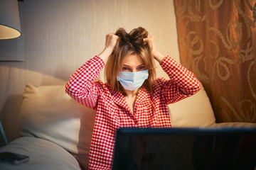 Young businesswoman in a medical protective mask works from home at the computer during self-isolation and quarantine. Virus coronavirus outbreak, flu epidemic and covid ncov novel. Stay home.
