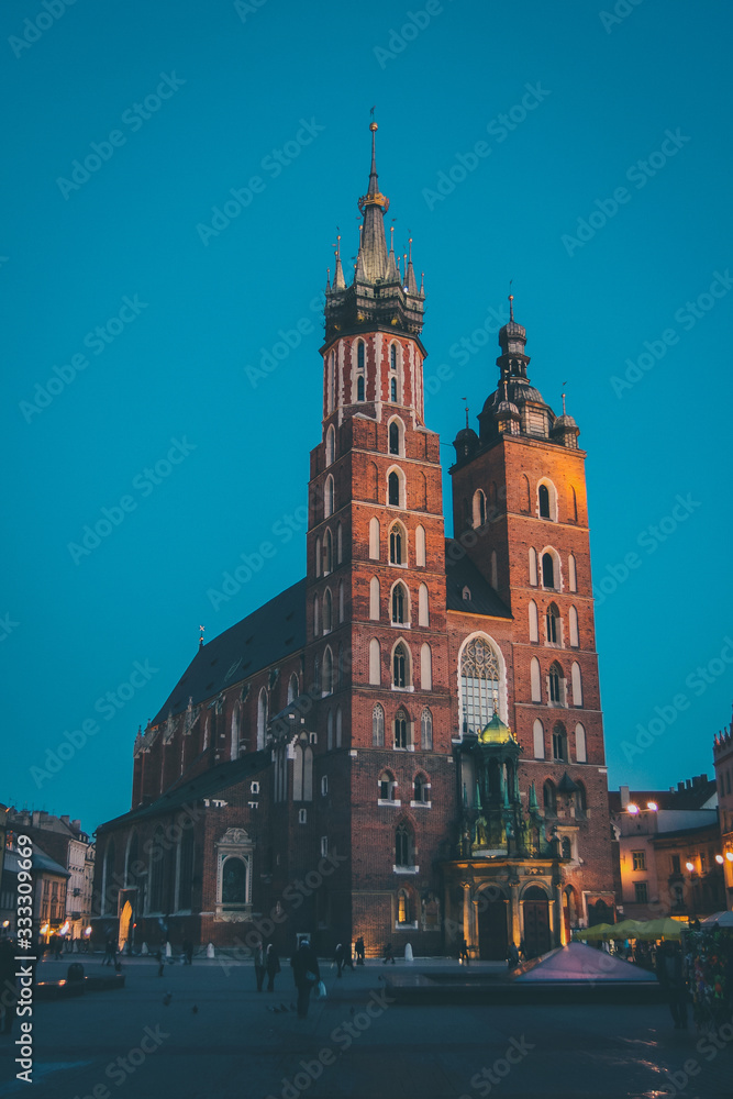 Sticker Mariacka bazylika or St. Mary Basilica in Krakow, Poland in beautiful evening light. Visible red brick towers and blue sky with some tourists around