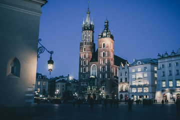 Naklejka premium Mariacka bazylika or St. Mary Basilica in Krakow, Poland in beautiful night setting and blue light. Visible red brick towers and blue sky with some tourists around