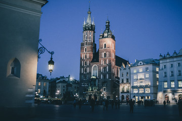 Mariacka bazylika or St. Mary Basilica in Krakow, Poland in beautiful night setting and blue light. Visible red brick towers and blue sky with some tourists around