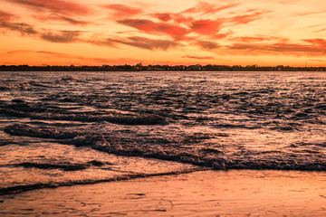 Obraz premium Sunset Colored Waves Crossing and Rippling, Pink Clouds in the Sky Behind