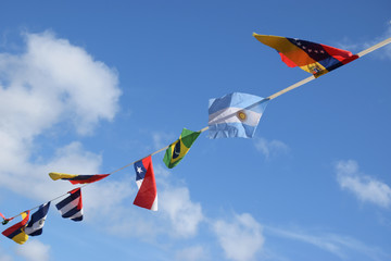 Flags of the world flutter in the breeze set agains a blue sky and fluffy white clouds