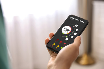 Man with smartphone checking pandemic data indoors, closeup. Coronavirus outbreak