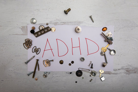 ADHD in red ink on white paper scattered random pieces of metal messy junk 