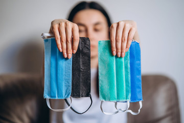 Female at home in quarantine time holding colorful protective medical masks to prevent virus...