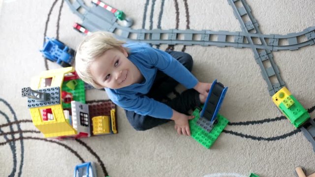 Adorable little boy playing with colorful plastic construction blocks at home, sitting on the floor, train going on railroad. Creative games for kids