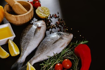 Fish seafood dorado, raw food on black background, nutrition lemon.