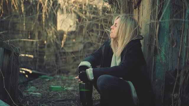 Depressed young woman drinks alcohol from a bottle and smokes. Drug use, addiction, social degradation and self-destruction concept 