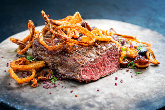 Traditional dry aged sliced roast beef with fried onion rings and potatoes served as closeup on a modern design plate