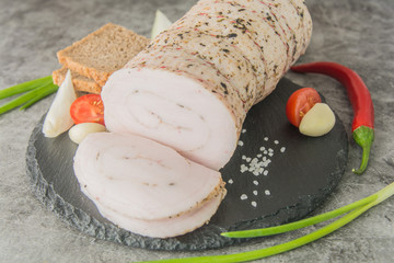 A large piece of white lard with spices covered in twine on a black slate with bread and...