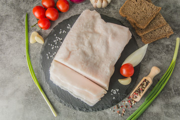 A large piece of white fat sprinkled with coarse salt, on black slate, with spices and herbs, top...