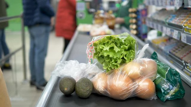 Girl at the checkout in the supermarket spreads foodstuffs in rubber gloves on the heading tape. Coronavirus infection protection.