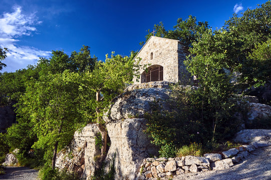 A stone, historic chapel on the rocky slope of a canyon in the Ardeche region in France.