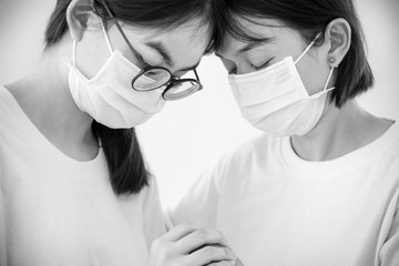 Two woman mother and daughter wear a mask to prevent the coronavirus outbreak with a sad feeling, Head against each other hold hands to comfort encourage to fight problems illness in black white color