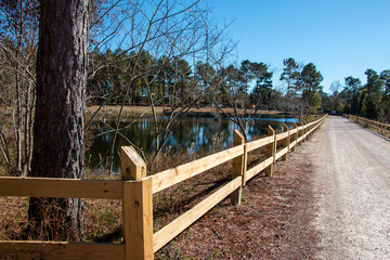 Obraz premium country dirt road by man made fish pond lake surrounded by trees
