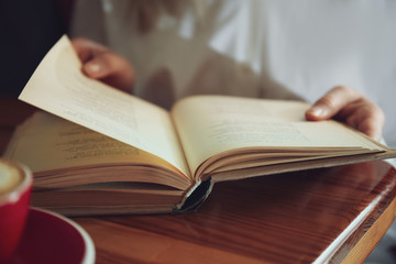 Woman reading book at table indoors, closeup