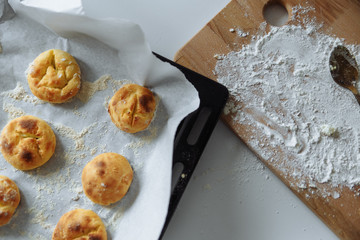 cookies on paper on a tray and a wooden board with flour on a white background.