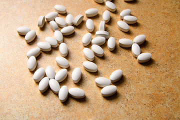vitamin D pills lie chaotically against a sand countertop