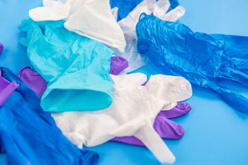 Pile of multicolored multiple medical latex gloves purple white blue and transparent with top view on a blue background. Coronavirus protection during quarantine.