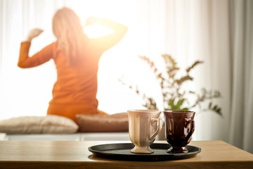 A woman at a sunny window on a wonderful morning behind a wooden table with warm tea