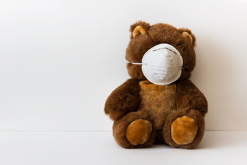 Brown kid plush toy teddy bear in white medical mask sitting on white background. Photo with copy blank space.