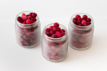 Concept of vitamin C doses. Superfood cranberries in small glass jars on white background.