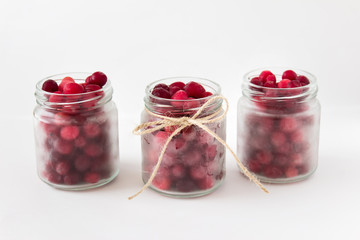 Three small glass jars with red berries cranberries and tied packthread rope on white background.
