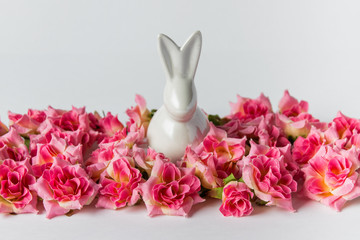 Decorative Eaester greeting card with white porcelain Easter bunny sitting in pink roses on white background.