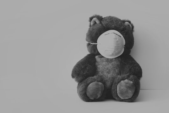 Concept with teddy bear and facial antivirus mask in sad gray dark black colors. Photo with blank space. 