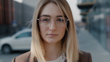 Extrime close up view of serious blonde caucasian young woman in glasses looking to the camera in the city spring sunlight outdoor successful female busines