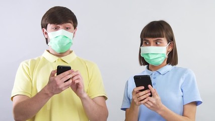 man and woman in sterile masks looking at phones and terrifiedly looking at each other